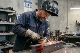 Homme en veste de travail soudant des poutres en acier